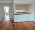 Open-plan space with a modern kitchen area featuring white cabinets, a black countertop, and a sink. The main area has polished wooden flooring and white walls.