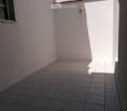 Empty outdoor patio with tiled flooring, white walls, and a small window on one side.