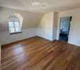 Empty attic room with wooden flooring, white walls, built-in closet, and a window with a view of the outside.