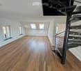 Completely empty room with wooden flooring, white walls, and a modern spiral staircase leading to an upper level. Skylights and windows provide natural light.