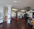 Large, open workshop or garage space with wooden flooring, white walls, and various tools and equipment. Includes a sink, tables, shelves, and a cart.