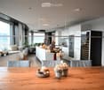 Open-plan living and dining area with a modern kitchen, large windows offering a scenic view, a wooden dining table with chairs, a sofa, and decorative items.