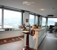 Modern kitchen with large windows offering a scenic view, featuring a kitchen island, cabinets, a sink, a stool, a chair, and a framed picture on the wall.
