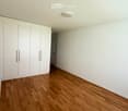 Empty room with light wooden flooring and white walls, featuring built-in white cabinetry on one side and a recessed ceiling light.