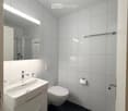 Modern bathroom with white tiles, a white sink with a chrome faucet, a toilet, a large mirror, and a towel rack.