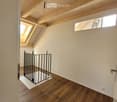 Empty attic room with wooden floors, exposed wooden beams, and skylights. A small black baby gate is placed on a white mat near the entrance.