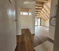 Empty hallway with wooden flooring, white walls, and exposed wooden beams in the ceiling. A small rug is placed near the doorway leading to another room.