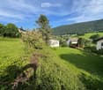 A lush green garden with well-maintained grass, bushes, and trees, surrounded by houses and a scenic mountain backdrop.