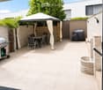 A modern outdoor patio with a tiled floor, a covered seating area with a table and chairs, a grill, a fire pit, and a covered barbecue area.