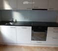 Modern kitchen with white cabinets, black countertops, stainless steel sink, and built-in oven.