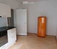 Modern kitchen with light wooden flooring, white cabinets, a black countertop, and a vintage-style orange refrigerator.
