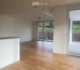 Empty room with wooden flooring, white walls, and large glass doors leading to an outdoor area.