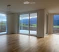 Empty room with wooden flooring, large windows, and sliding glass doors leading to a patio with a scenic mountain view.
