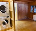 Wooden floor and walls, with a washing machine and dryer unit placed on a raised platform, and a small window letting in natural light.