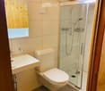 Modern bathroom with a white sink, toilet, and glass-enclosed shower. The room features light-colored tiles and wooden accents.