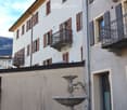 white building with brown shutters, balconies, fountain in front