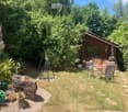 A serene garden area with a wooden cabin, outdoor seating, a fire pit, and lush greenery.