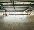 Large, empty industrial-style room with concrete floors, exposed metal beams, and large windows allowing natural light. Minimal furnishings, including a few crates and storage boxes.