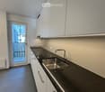 Modern kitchen with white cabinets, dark granite countertop, stainless steel sink, and a door leading to a balcony.