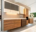 Modern bathroom with wooden cabinets, white sinks, and a large mirror with LED lighting. Features a sleek design with multiple sinks and a toilet in the background.