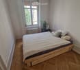 Cozy bedroom with wooden herringbone flooring, a single bed with white bedding, a nightstand with a lamp and potted plant, and a radiator beneath the window.