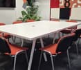 A modern meeting room with a white rectangular table surrounded by red and black chairs, a potted plant, and colorful wall art.
