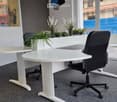 Modern office space with white desks, black office chairs, and a small potted plant on the desk.