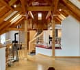 Open-plan living and dining area with exposed wooden beams, a staircase leading to an upper level, a modern kitchen island, and a cozy seating area with a fireplace.