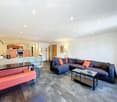 Modern living room with a large sectional sofa, coffee tables, a bench, and a small kitchen area with appliances.