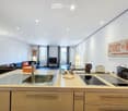 Modern open-plan living and kitchen area with a sofa, coffee table, television, and a kitchen island with a sink, stove, and various appliances.