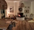 Cozy living and dining area with a central fireplace, wooden dining table, sofa, and decorative elements including a wreath and picture frames.