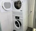 Modern bathroom with a private washing machine and dryer unit, white tiled walls, and dark tiled floor.
