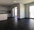 Empty kitchen with white cabinets, dark tiled floor, and large sliding glass doors leading to a balcony.