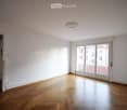 Empty room with wooden parquet flooring, white walls, large sliding glass doors leading to a balcony, and a ceiling light fixture.