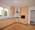 Modern kitchen with light wooden cabinets, stainless steel sink, stove, microwave, and range hood. Large windows provide natural light.