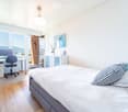 Bright bedroom with a large bed, desk with chair, and a view of the mountains through large windows and a sliding door.