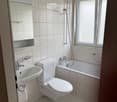 Modern bathroom with white tiles, a sink, toilet, bathtub, and a window with blinds.