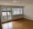 Empty room with wooden flooring, large windows with blinds, radiator, and a sliding glass door leading to a balcony area.