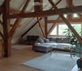 Spacious living room with wooden beams, large windows, grey sectional sofa, coffee table, ottoman, and potted plants.