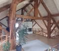Loft-style living room with exposed wooden beams, fireplace, sofa, coffee table, potted plants, and decorative vase.