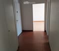 Empty hallway with tiled floor, white walls, and a door leading to a bright area.