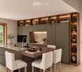 Modern kitchen with a central island, built-in cabinets, and a dining area. Features include a sink with a modern faucet, a wooden dining table with four chairs, and decorative items such as books, vases, and potted plants on the island and shelves.