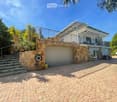 Two-story house with a stone facade, garage, balcony, and outdoor seating area. The entrance features stone steps leading up to the house.