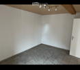 Empty room with white walls, grey tiled floor, and a wooden ceiling with track lighting. No furniture or equipment present.
