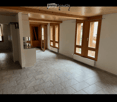 Empty room with tiled floor, wooden ceiling, large windows, and open doors leading to another area.