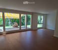 Empty room with wooden flooring, large windows, and sliding glass doors leading to a patio area.