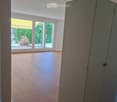 Empty room with wooden flooring, large sliding glass doors leading to a patio, and a view of greenery outside.