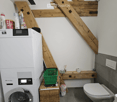 Bathroom with a washing machine, toilet, wooden shelf, and a small woven basket on the floor.