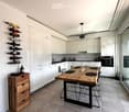 Modern kitchen with white cabinets, a wooden dining table, wine rack, and a large window.