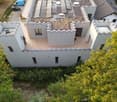 Modern two-story building with a flat roof and decorative battlements, surrounded by greenery and trees.